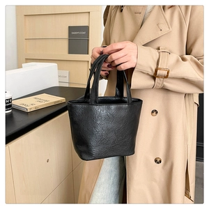 Detail of a chic black pleated leather bucket bag with top handles shown in a lifestyle setting