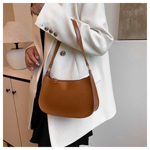 Brown leather crescent hobo bag with gold zipper detail worn over a white suit jacket