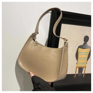 Detail shot of beige crescent hobo bag showing glossy patent leather texture and zipper