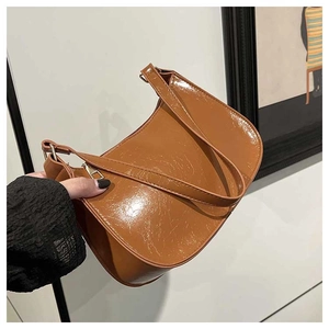 Detail of a brown glossy patent leather crescent shoulder bag with smooth metal zipper