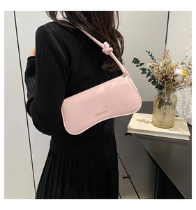 Close-up of pink leather shoulder bag featuring unique knotted strap and gold branding