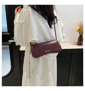 Detail of a shiny deep purple leather shoulder bag on a model wearing a white coat