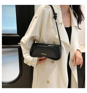 Close-up of black glossy leather underarm bag with knot detail and gold buckle