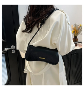 Close-up of black glossy leather underarm bag with gold logo and sleek curved design