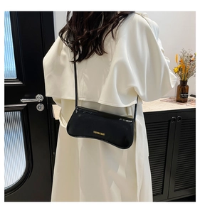 Glossy black patent leather underarm bag worn by a model in a minimalist setting