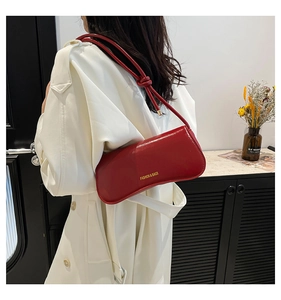 Detail of red patent leather underarm bag with gold lettering and knotted shoulder strap