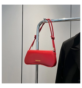 Detail of red shoulder bag with gold lettering hanging on a metal rack next to a black blazer