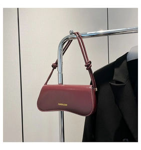 Close-up of burgundy leather underarm bag with gold logo and knotted strap detail