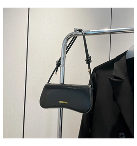 Detail of black glossy baguette bag featuring a knotted shoulder strap and gold lettering