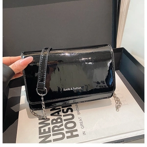 Detail view of black glossy patent leather crossbody bag with silver chain and white logo