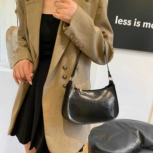 Black glossy pleated baguette bag with gold hardware worn by model in olive blazer