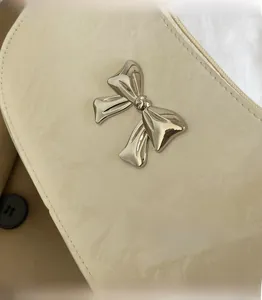 Close-up of a cream-colored leather handbag featuring a large 3D silver metal bow detail