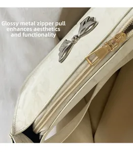 Detailed macro view of white shoulder bag featuring smooth gold zipper and silver bow charm
