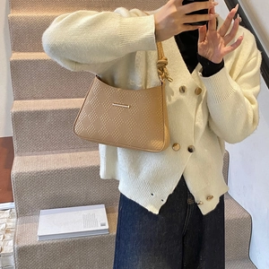 Close-up of light brown shoulder bag with woven texture and gold buckle on a model