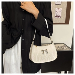 Detail of white pleated crescent bag featuring a silver metal bow and shoulder strap