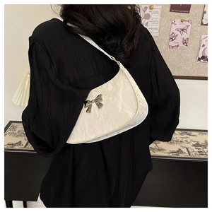 Detailed view of the white crescent underarm bag with silver bow on a person