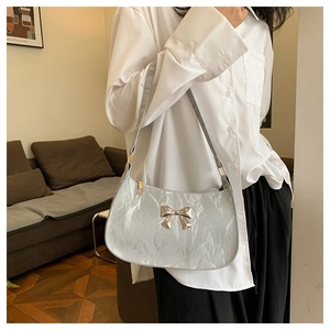 Silver-gray pleated underarm bag with a golden bow detail worn in a cozy indoor setting
