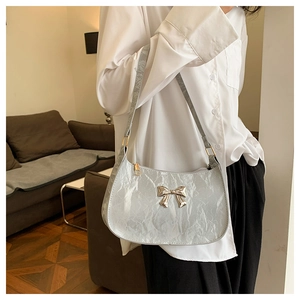 Detail of silver metallic shoulder bag featuring a glossy texture and butterfly metal buckle