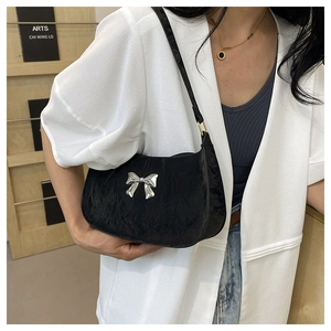 Close-up of black pleated underarm bag with a silver metal bow accent on model