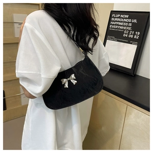Detail of black underarm bag with silver butterfly bow accessory on model shoulder
