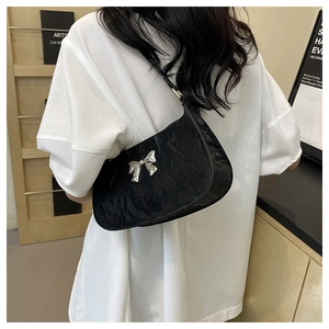 Detail of black crescent shoulder bag with silver bow on model wearing white T-shirt
