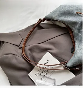 Dettaglio della trama in denim blu lavato e dei cinturini in pelle marrone della borsa