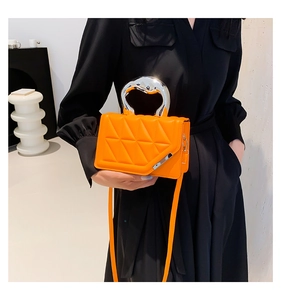 Detail of bright orange quilted crossbody bag with a modern silver irregular metal handle