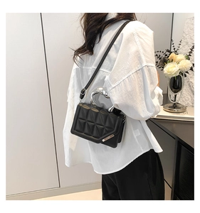 Detail of black quilted shoulder bag featuring unique silver U-shaped metal handle and strap