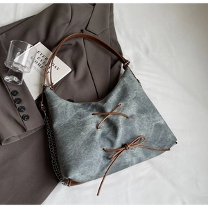 Dettaglio borsa tote in denim grigio con manici in pelle marrone, fiocco e catena