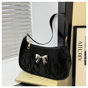 Detail of black pleated PU leather crescent bag with a silver metallic bow decoration