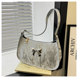 Detail of silver pleated crescent bag featuring a metallic bow and gold hardware accents