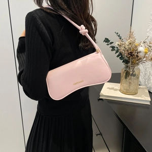 Pink faux leather shoulder bag with knot strap and gold lettering worn by model