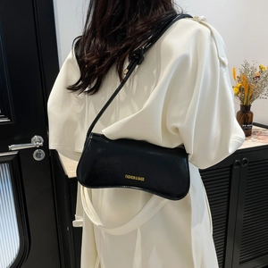 Chic black crescent underarm bag in glossy leather worn by a model in a white coat
