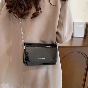 Glossy black patent leather flap crossbody bag with silver chain strap and white text