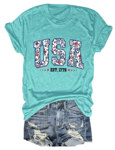 Flat lay of USA EST 1776 graphic tee in turquoise paired with distressed denim shorts