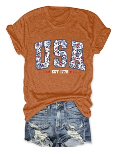 Close-up of rust red USA EST. 1776 graphic tee with floral pattern and denim shorts