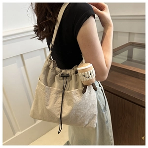 Detail of a beige nylon bucket bag with drawstring closure and a plush coffee cup charm
