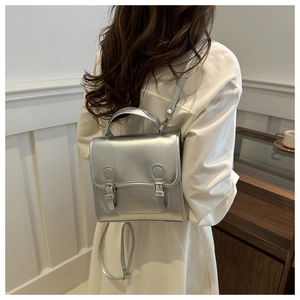 Detail shot of a trendy silver metallic mini backpack worn over a white outfit