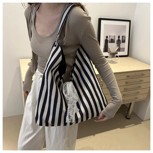 Close-up of a striped canvas tote bag with white lace bow detail worn by a model