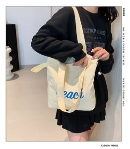 Detail of off-white nylon tote bag showing peach lettering and drawstring side accents
