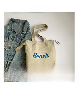 Detailed top view of beige canvas tote bag with blue Beach lettering and denim jacket