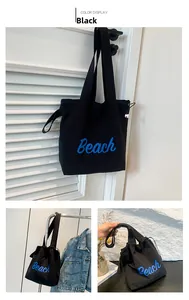 Detail view of black canvas tote bag with blue Beach lettering and drawstring closure