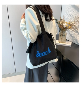 Detail of black drawstring tote bag with blue Beach lettering worn over the shoulder