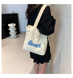 Detail view of the beige canvas tote bag with blue Beach lettering and pleated texture