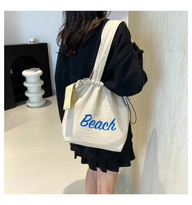 Detail of cream canvas tote bag featuring blue Beach embroidery and drawstring closure