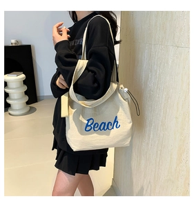 Detail of off-white canvas tote bag featuring blue Beach lettering and side-view silhouette