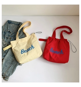 Detail view of canvas beach tote bag with blue Beach lettering and drawstring closure