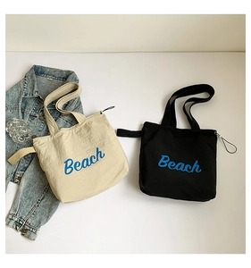 Flat lay of beige and black canvas tote bags with Beach lettering and denim jacket