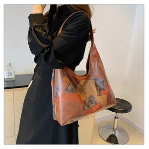 Model wearing a large patchwork leather tote bag with contrast stitching in a warm room