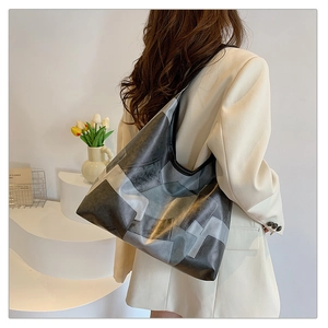 Detail view of large grey color-block patchwork tote bag on shoulder with wide strap